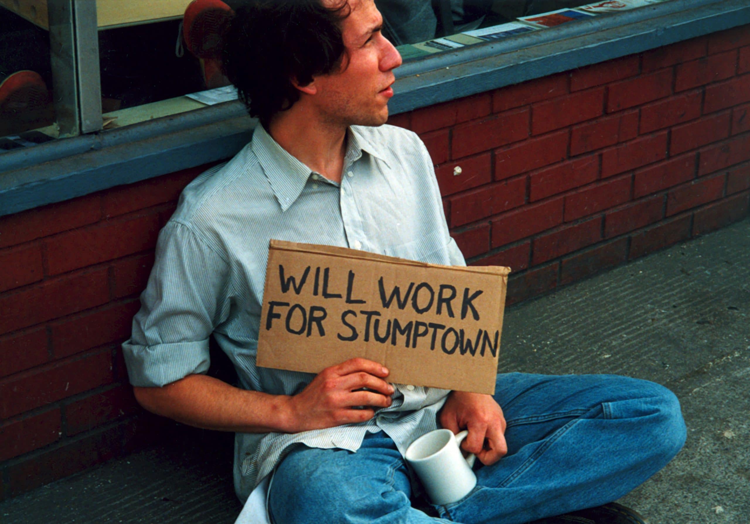 Raymond holding a signs that says "WILL WORK FOR STUMPTOWN" - part of an early art project.