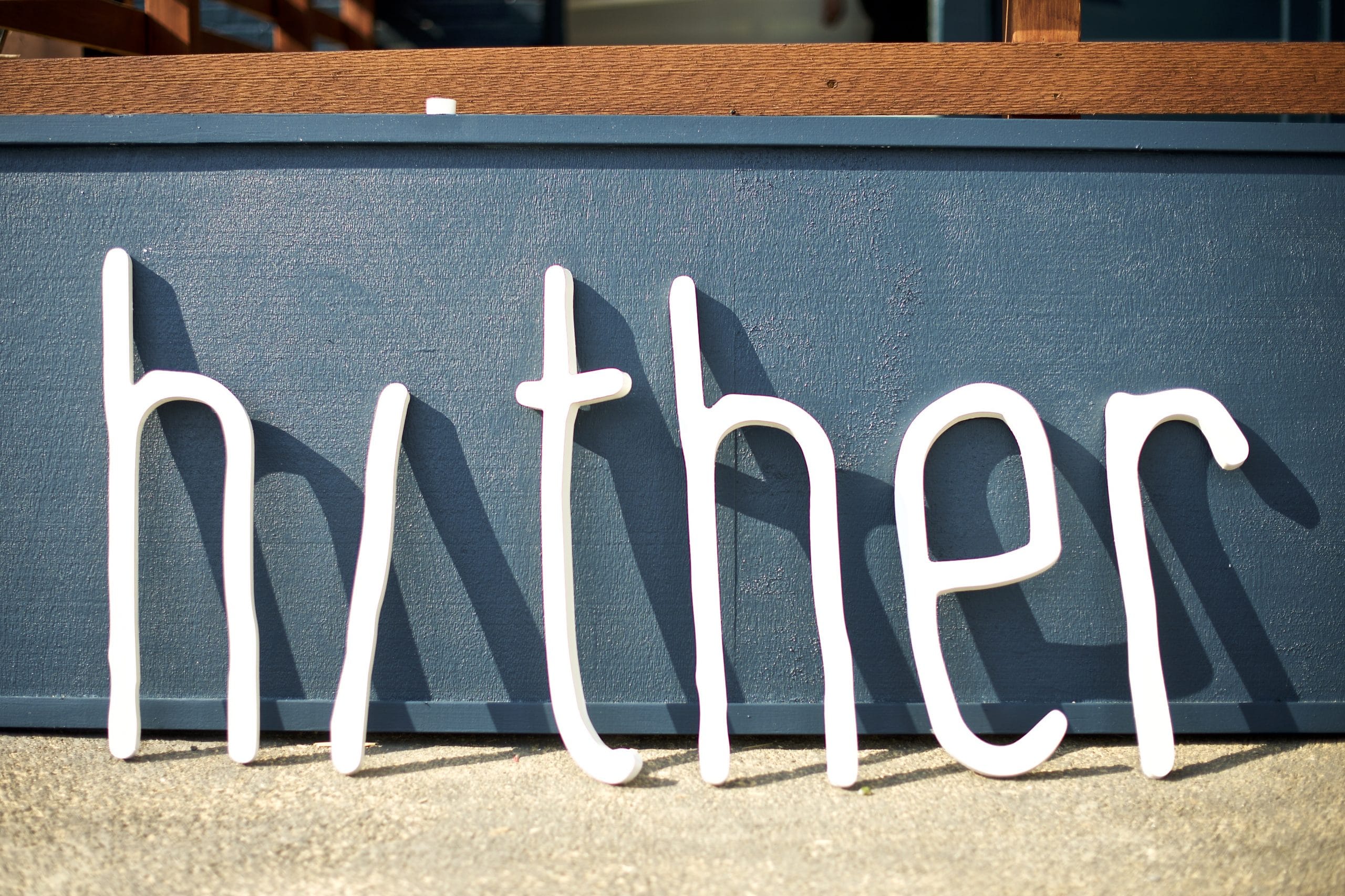 All the letters from the Hither Coffee + Goods sign leaning against a wall