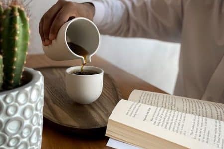 Person pouring coffee and reading a book at Stanza